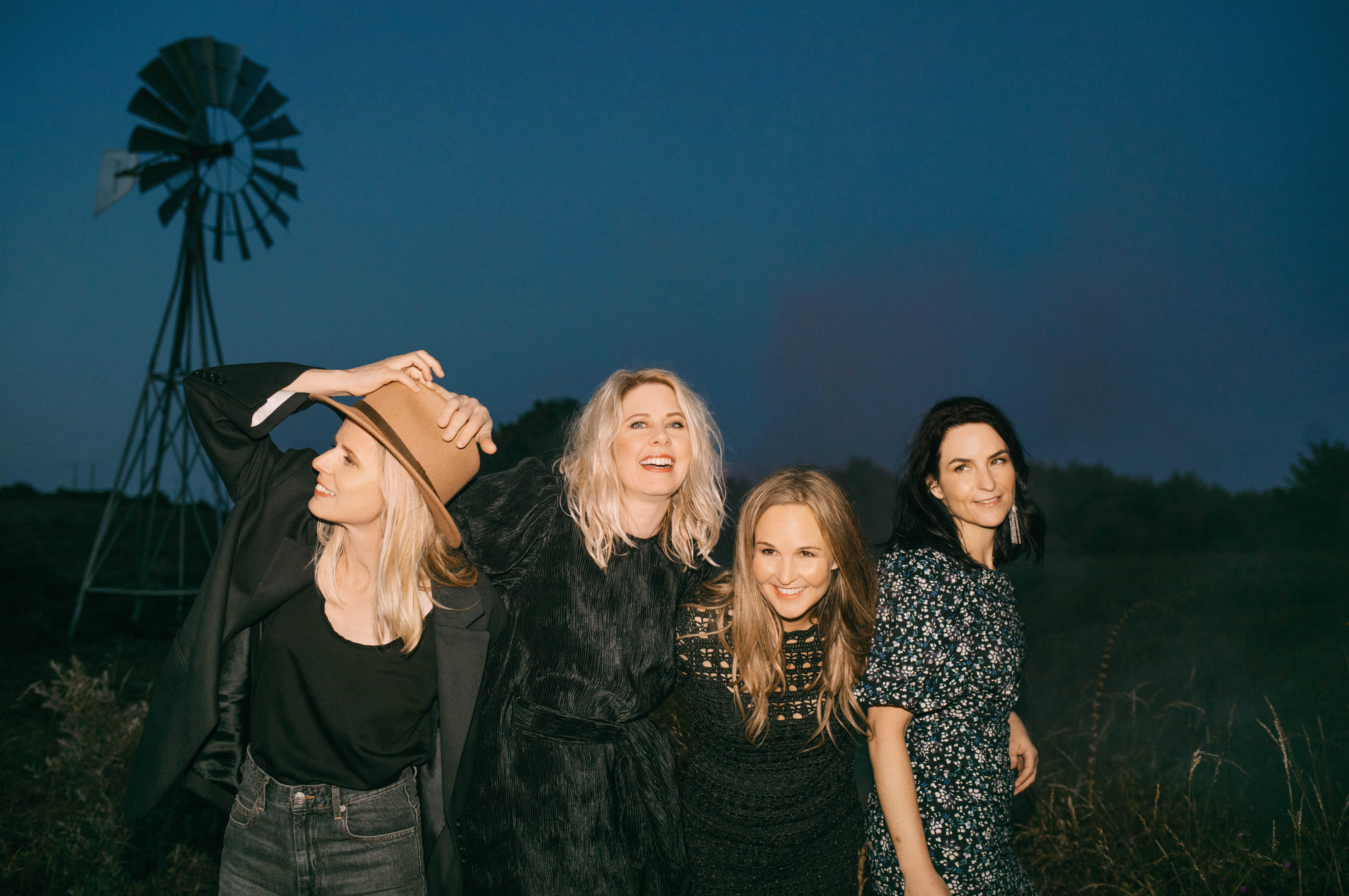 Five women posing together outdoors at dusk with a windmill in the background.